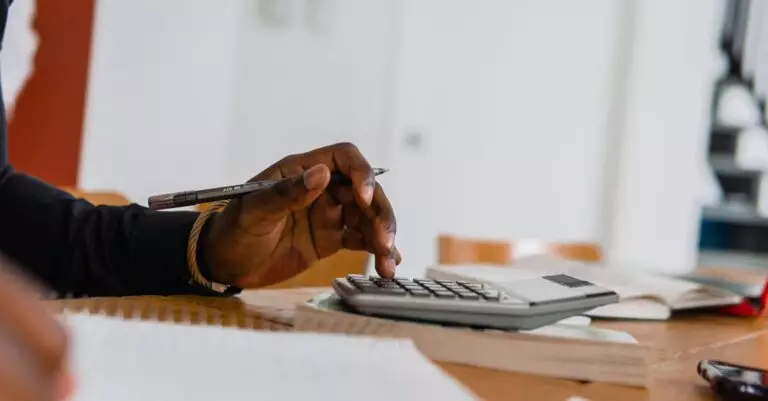 Close-up of a person using a calculator and pen for financial work at a desk.